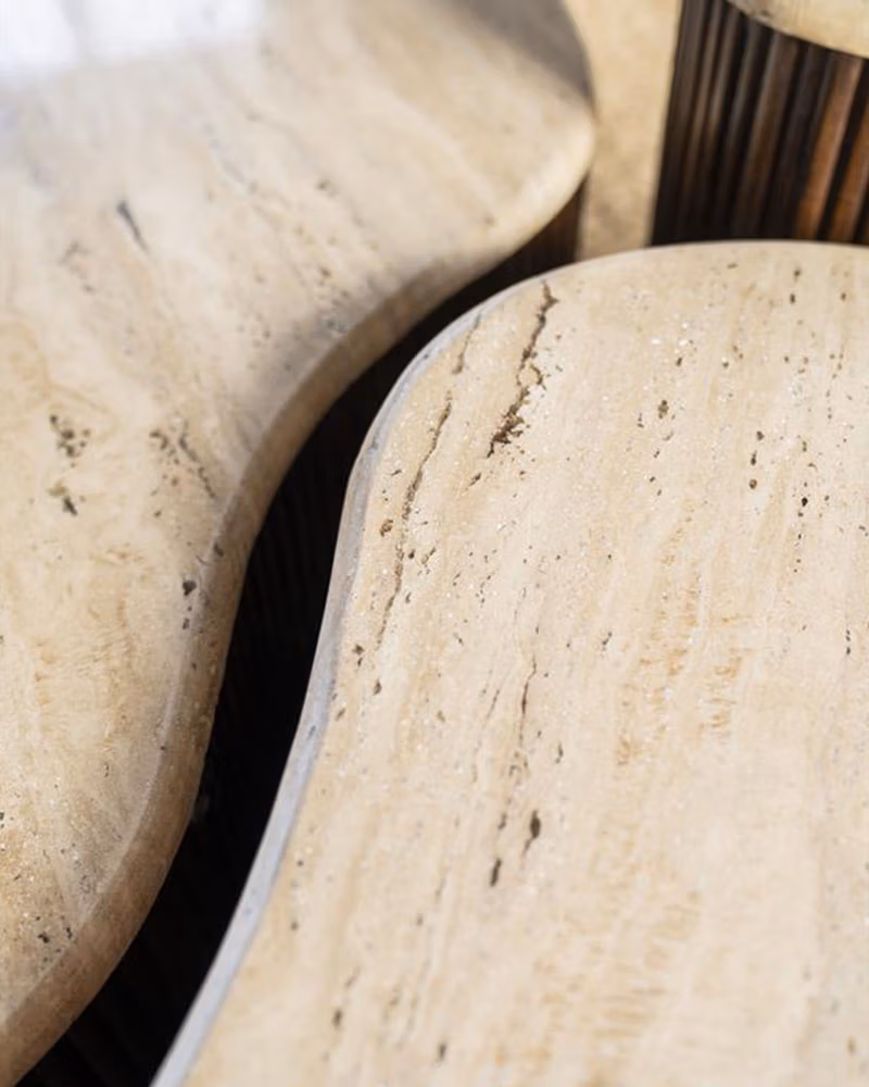 Close-up van drie overlappende, gebogen beige stenen of marmeren organische tafelbladen met natuurlijke adering en gladde randen, waardoor een abstract, organisch patroon ontstaat.