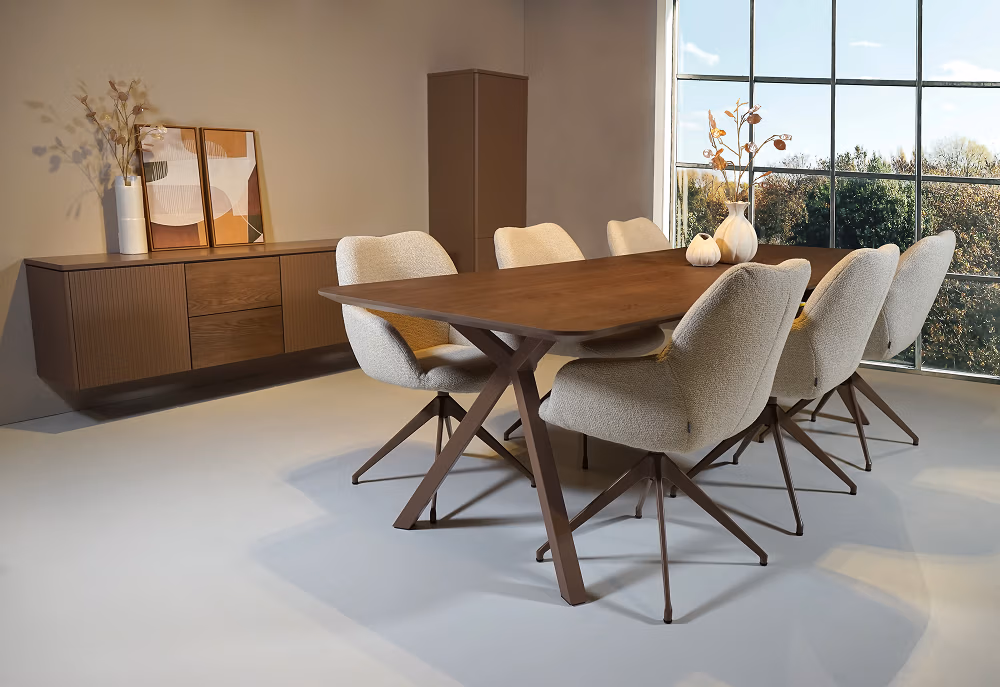 Een moderne eetkamer met een houten tafel, acht beige stoelen met kussens, een dressoir met abstracte kunst en vazen en grote ramen die natuurlijk licht binnenlaten.