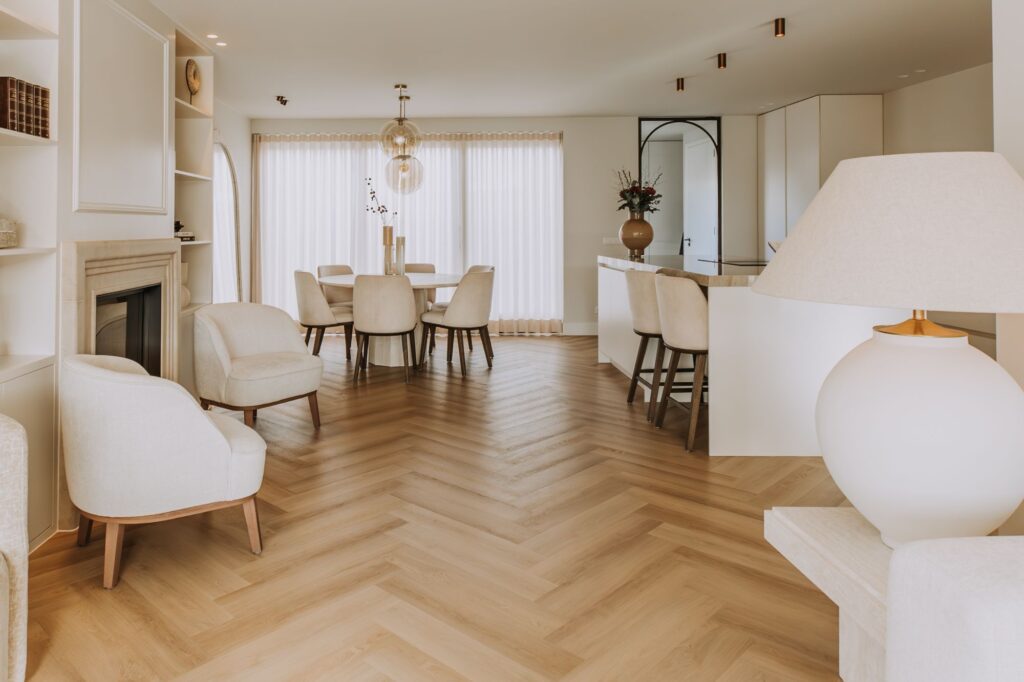 Moderne open woon- en eetruimte met lichthouten visgraatvloeren, witte muren, beige gestoffeerde stoelen en een strak keukeneiland - perfect voor een minimalistisch interieur met grote ramen en transparante gordijnen.