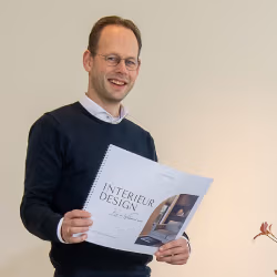 Evert van Wolfswinkel staat binnen met een open interieurmagazine en lacht naar de camera.